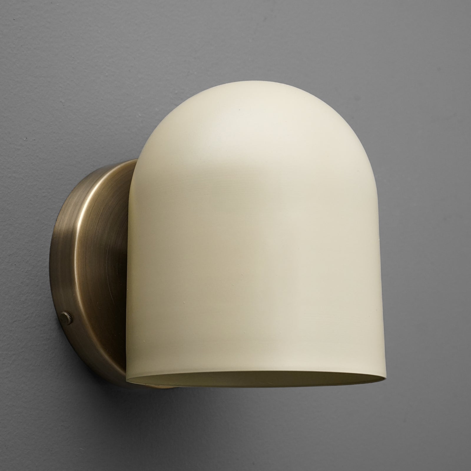 Antique brass wall sconce with smooth cream glass shade mounted on gray wall. - SCONCE MODEL NO. 2424