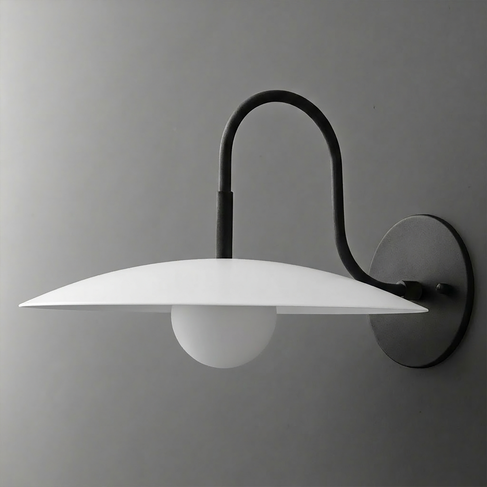 Black metal wall sconce with curved arm, flat white disc shade, and round frosted bulb. - SCONCE MODEL NO. 9171