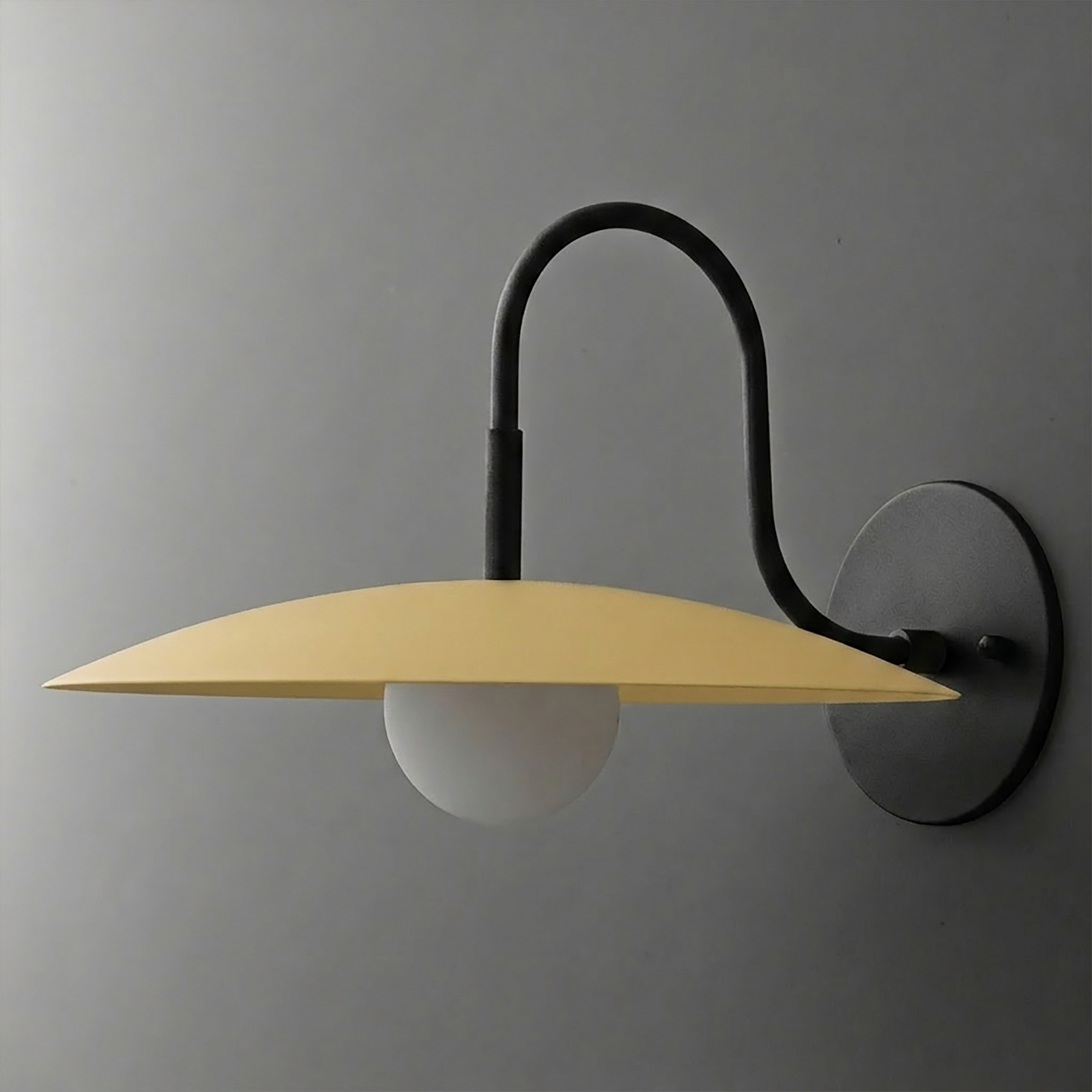 Wall-mounted sconce with matte black curved arm, round base, and wide flat yellow metal shade over frosted globe bulb. - SCONCE MODEL NO. 9171