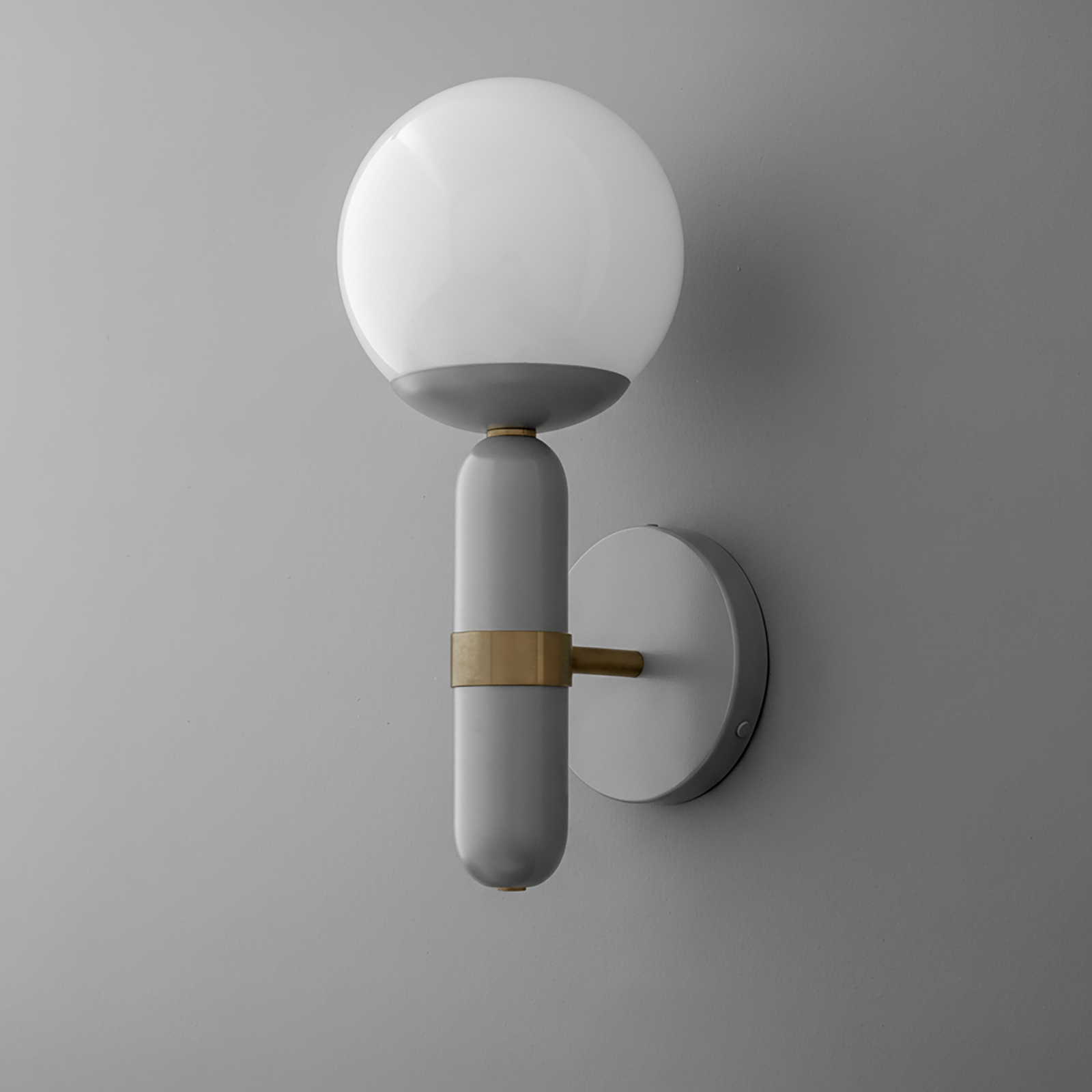 Wall sconce with round white glass shade and matte gray cylindrical base with brass accent on gray wall. - SCONCE MODEL NO. 4786