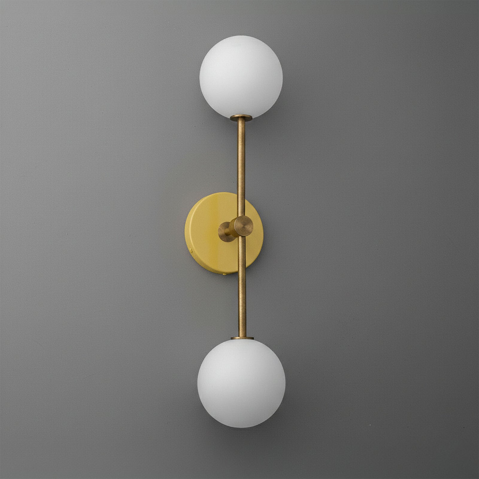 Raw brass double globe wall sconce with frosted white glass shades on gray background. - SCONCE MODEL NO. 9776
