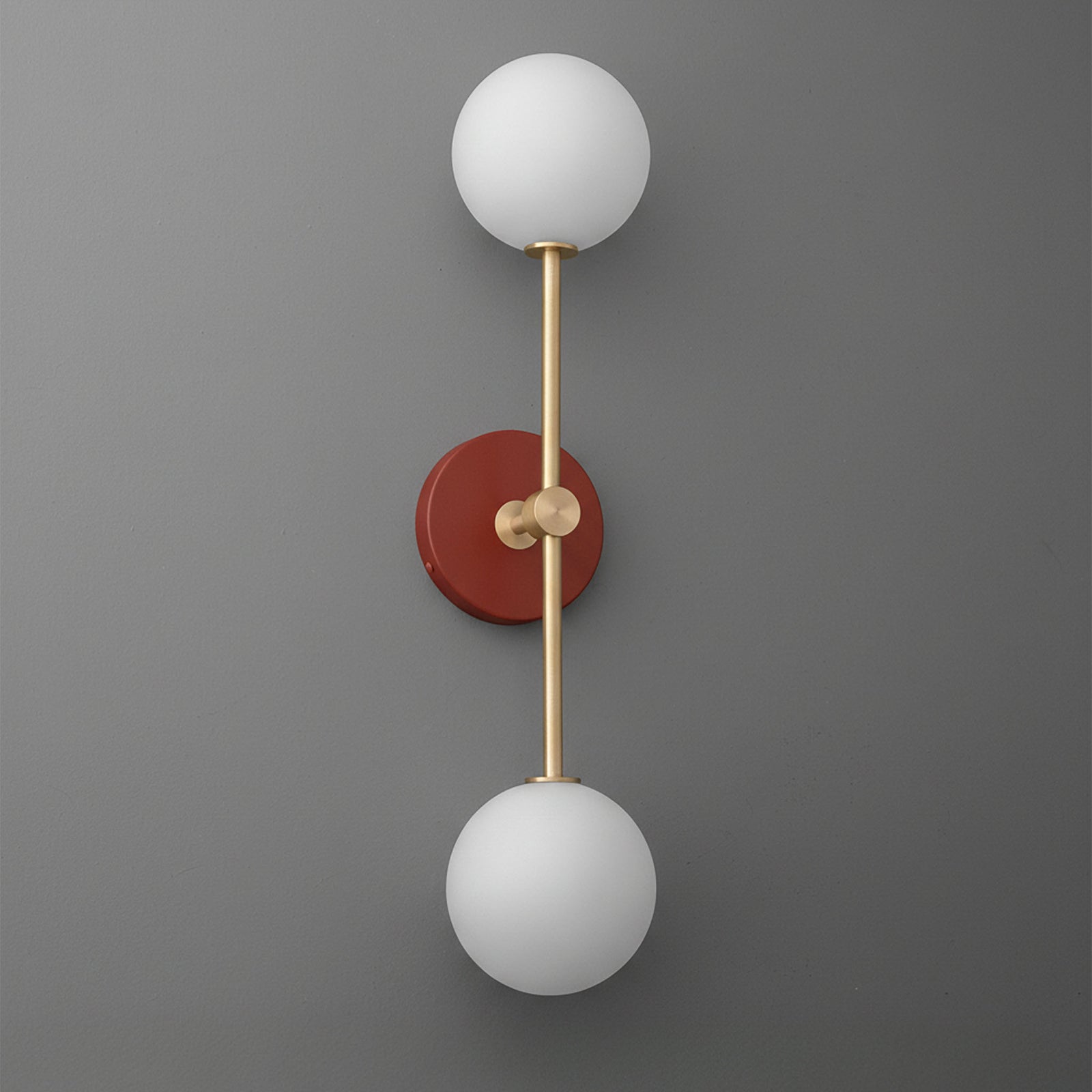 Raw brass double globe sconce with brick red round backplate on gray wall. - SCONCE MODEL NO. 9776