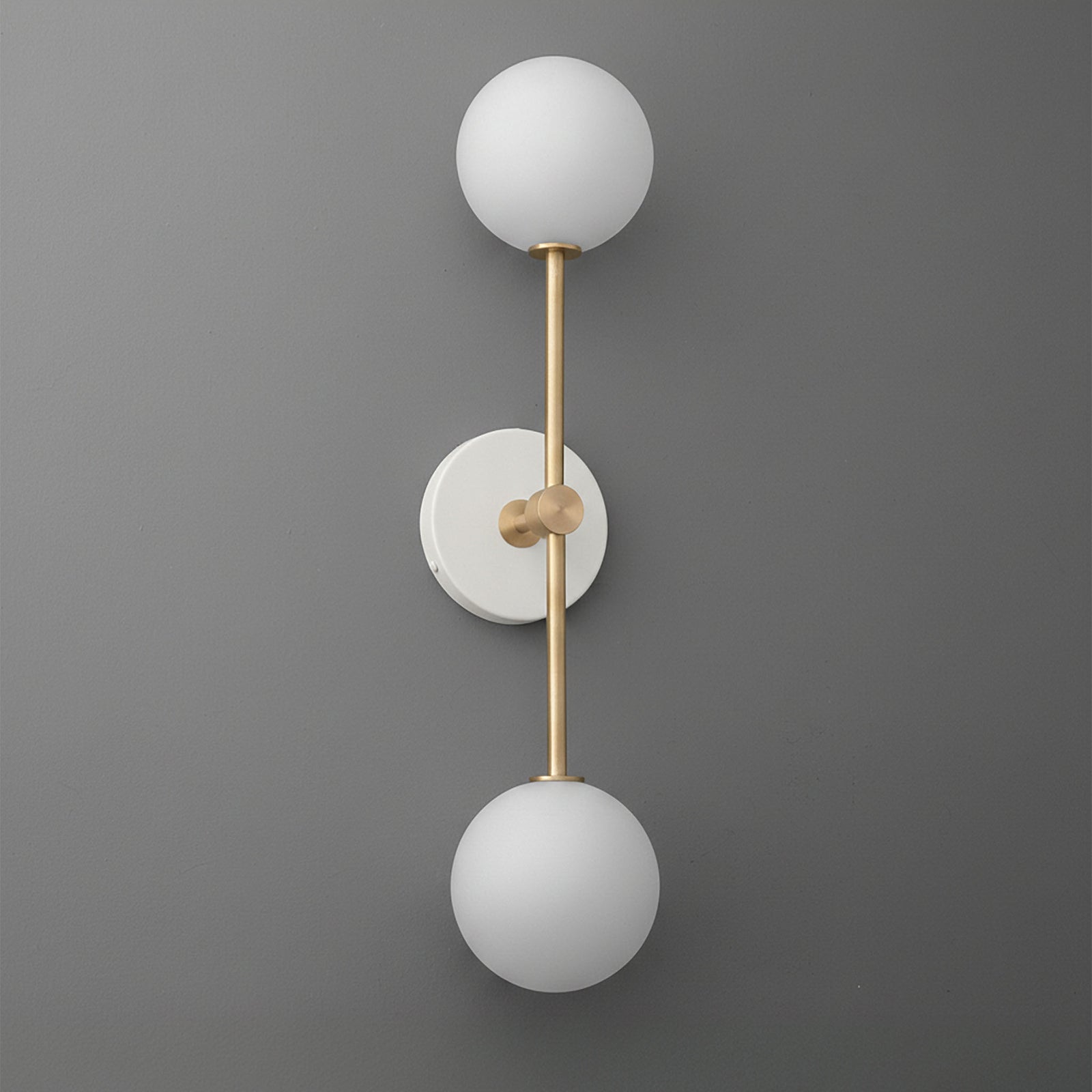 Modern double globe wall sconce with raw brass finish and frosted white glass shades on matte gray wall. - SCONCE MODEL NO. 9776