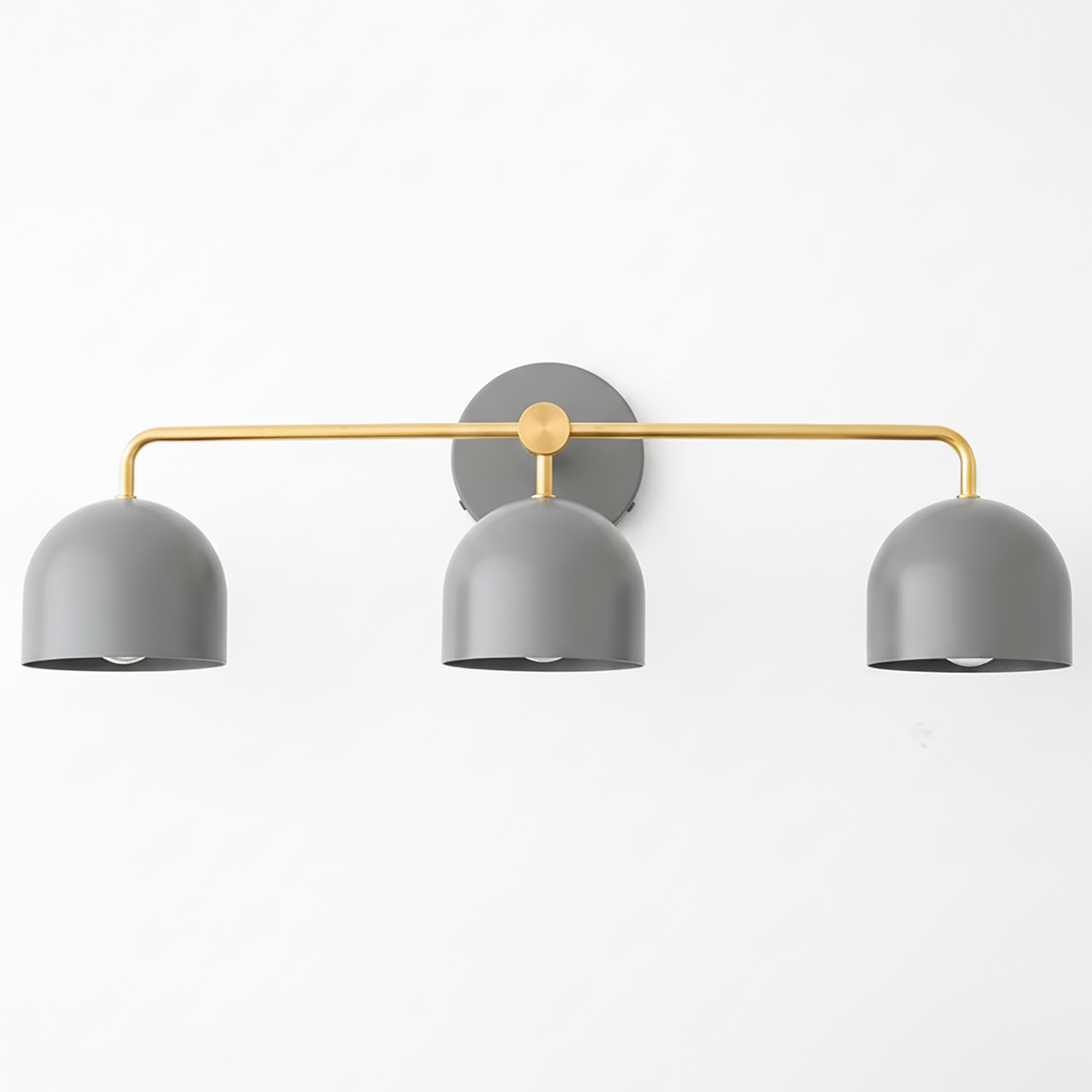 Mid-century modern vanity light with three matte gray dome shades and a gold horizontal bar mounting on a round gray wall. - VANITY LIGHT MODEL NO. 7456
