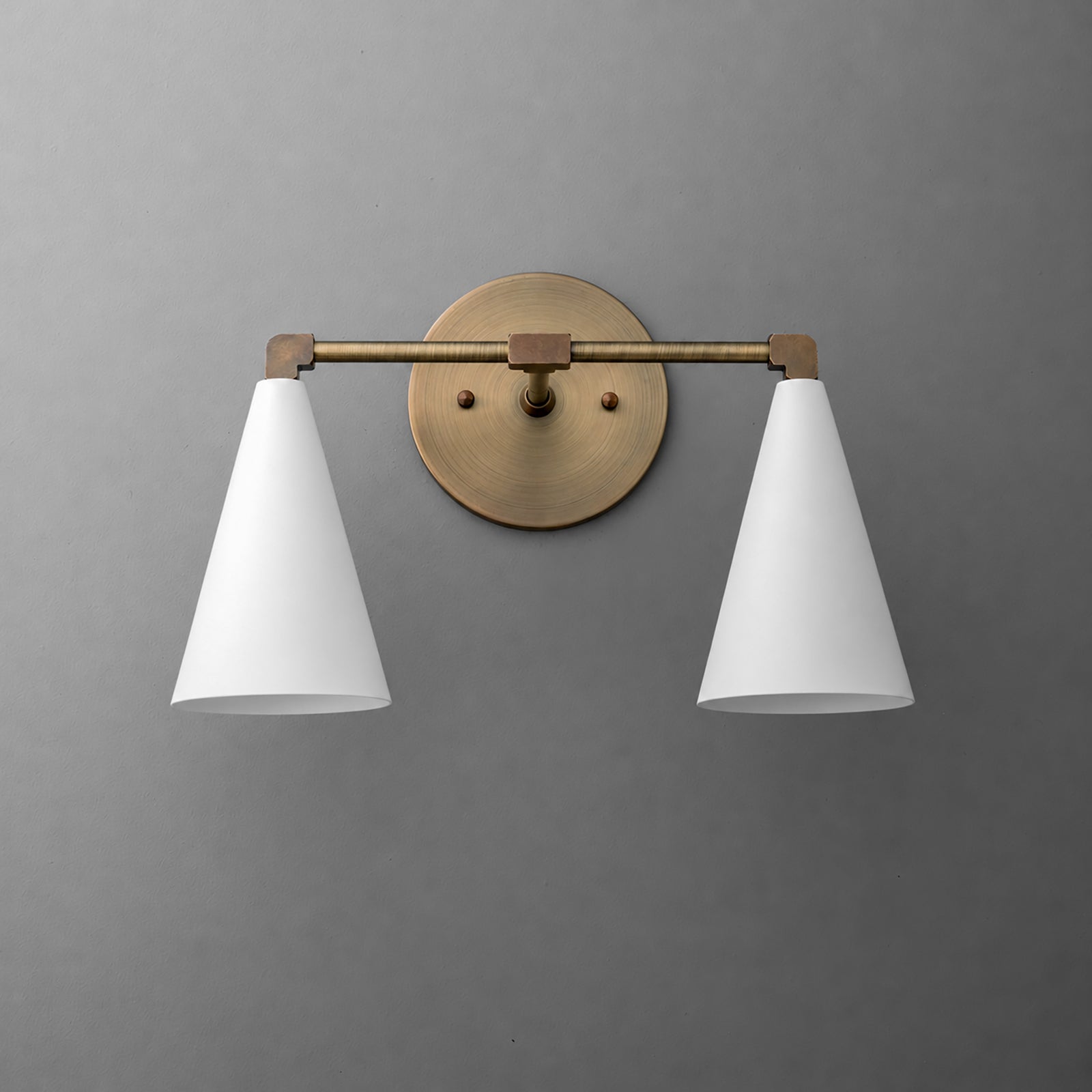 Two-light vanity light in Antique Brass with White cone shades on a straight arm and a round wall plate. - VANITY LIGHT MODEL NO. 1184