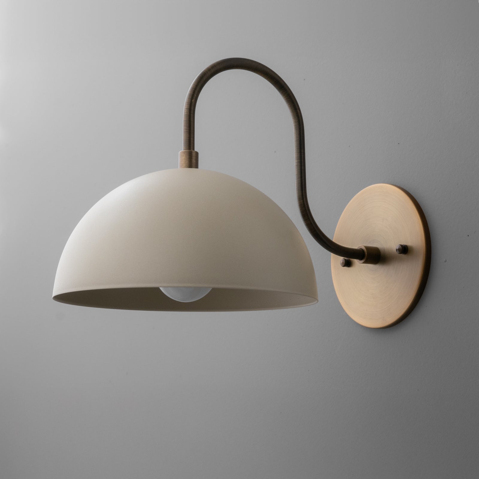 Wall sconce with matte cream dome shade and curved antique brass arm mounted on round brass backplate. - SCONCE MODEL NO. 9092
