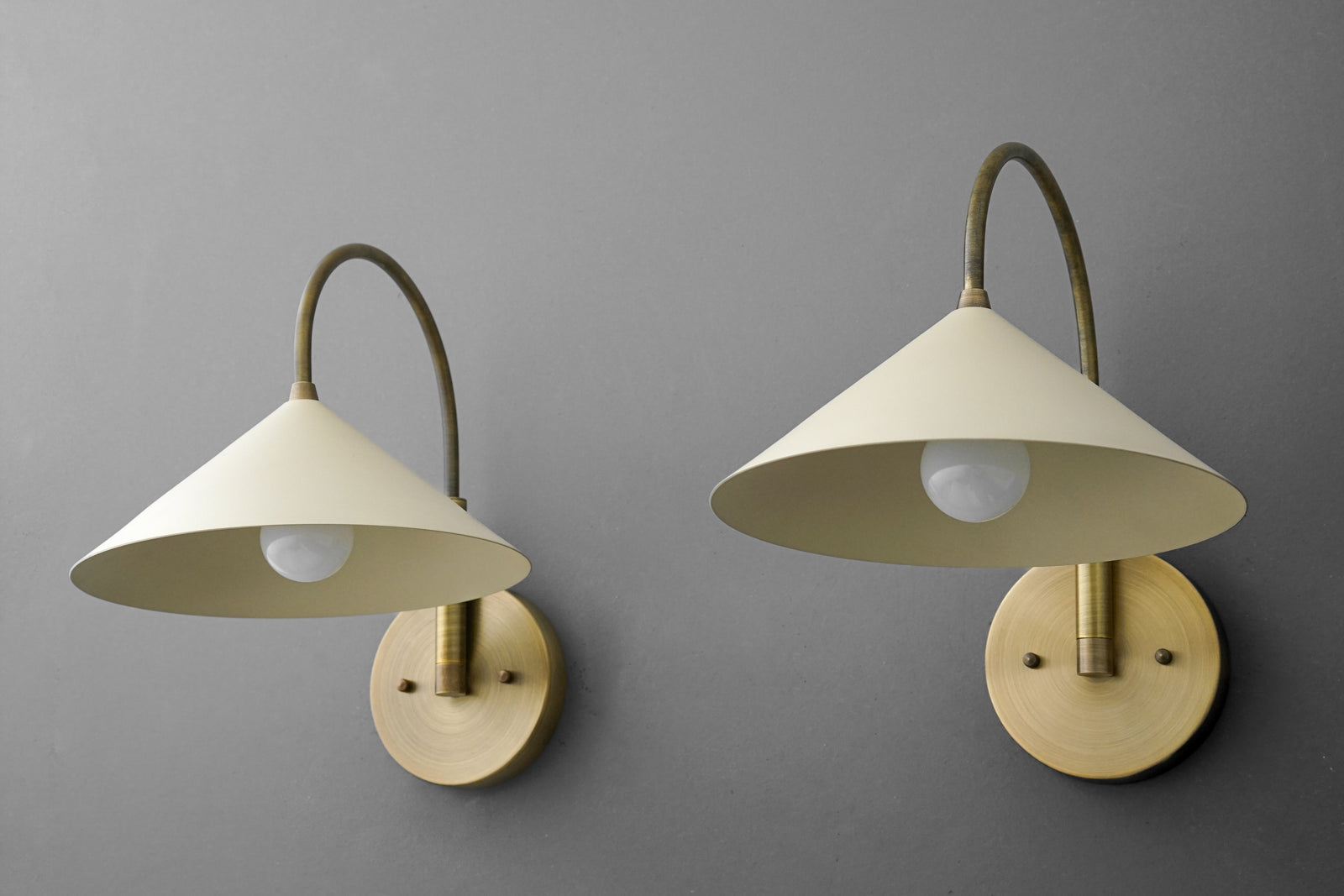 Antique brass wall sconce with cream conical shade and exposed bulb on gray wall, two sizes. - Sconce Model No. 1583