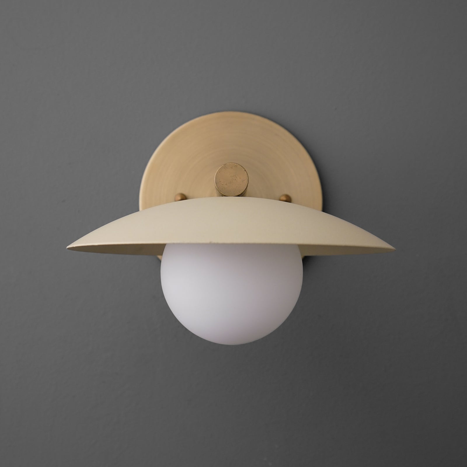 Minimalist wall sconce with antique brass finish and cream wide metal shade over white globe bulb. - SCONCE MODEL NO. 9875