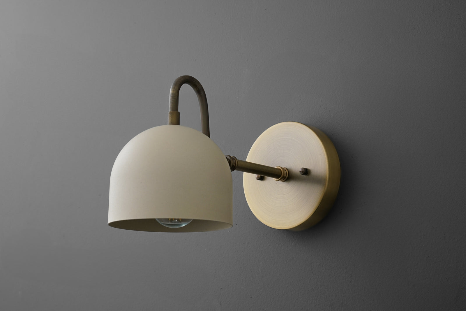 Antique brass wall sconce with cream dome shade and round backplate on gray wall. - SCONCE MODEL NO. 3628