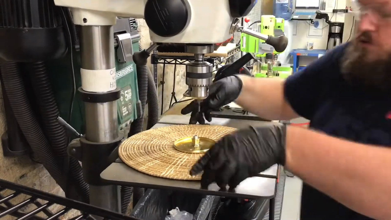 A Peared maker at the drill press lining up a woven rattan shade and a brass ring in the Chillicothe workshop