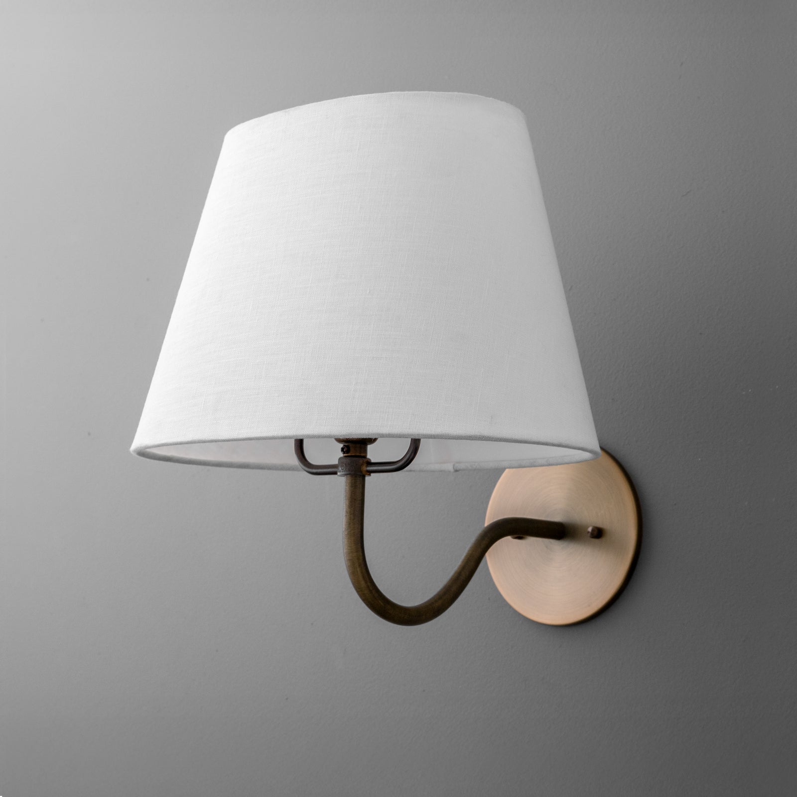 Wall-mounted sconce with antique brass arm and round base, fitted with a white fabric tapered shade. - SCONCE MODEL NO. 0303
