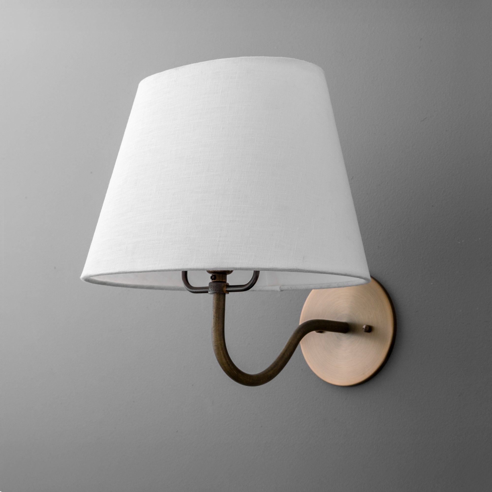 Wall-mounted sconce with antique brass arm and round base, fitted with a white fabric tapered shade. - SCONCE MODEL NO. 0303