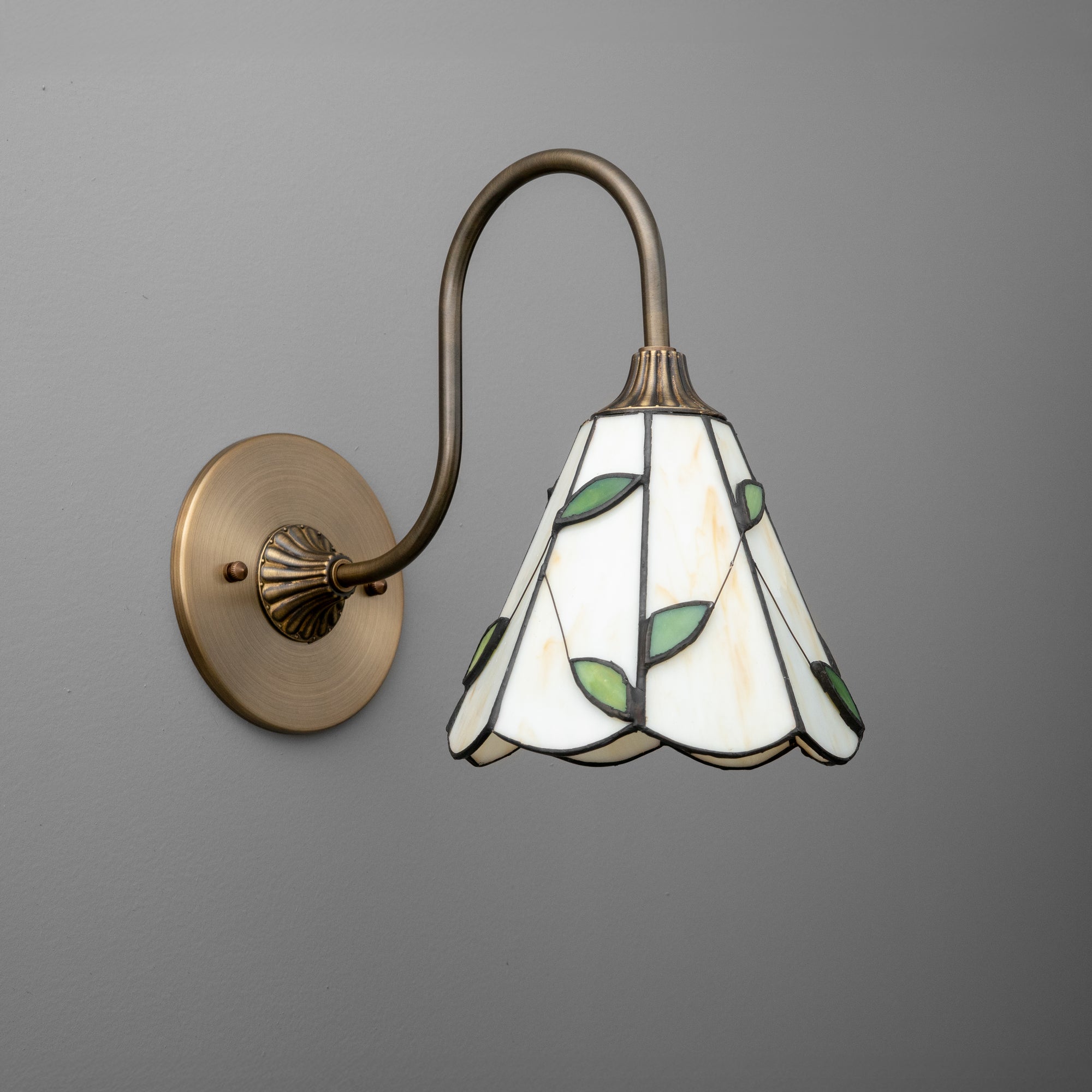 Wall sconce with antique brass finish and stained glass shade featuring green leaf accents. - SCONCE MODEL NO. 1053