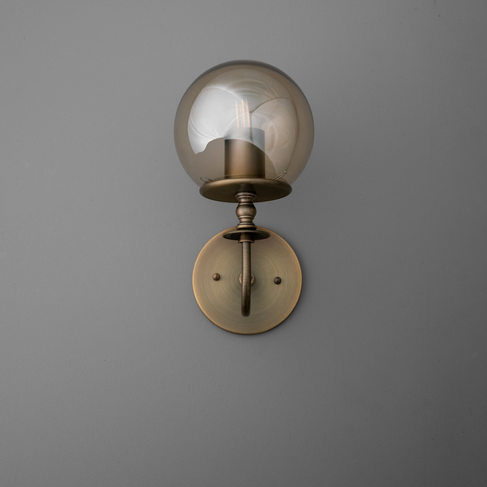 Wall sconce with antique brass finish, featuring a round backplate and a smoky glass globe shade. - SCONCE MODEL NO. 1029