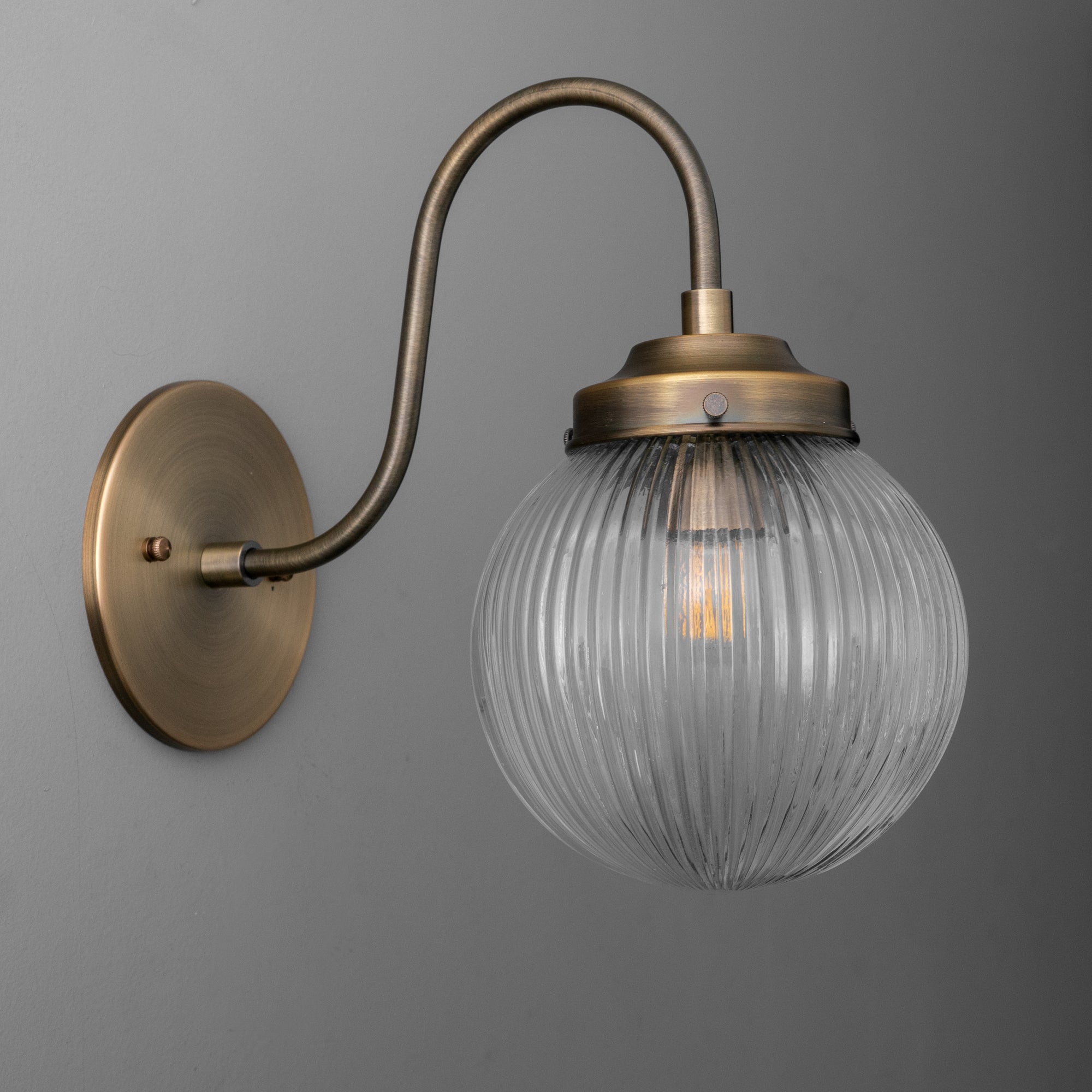 Antique brass wall sconce with curved arm and ribbed clear glass globe shade. - SCONCE MODEL NO. 0691