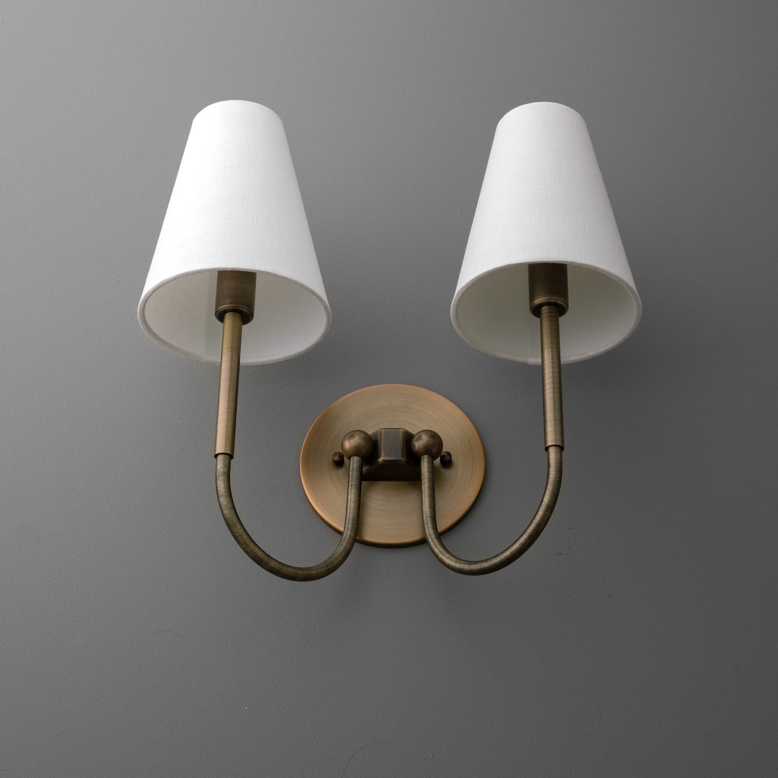 Two-light sconce in Antique Brass seen from below, showing the curved arms and the inside of the tapered linen shades. - SCONCE MODEL NO. 1111