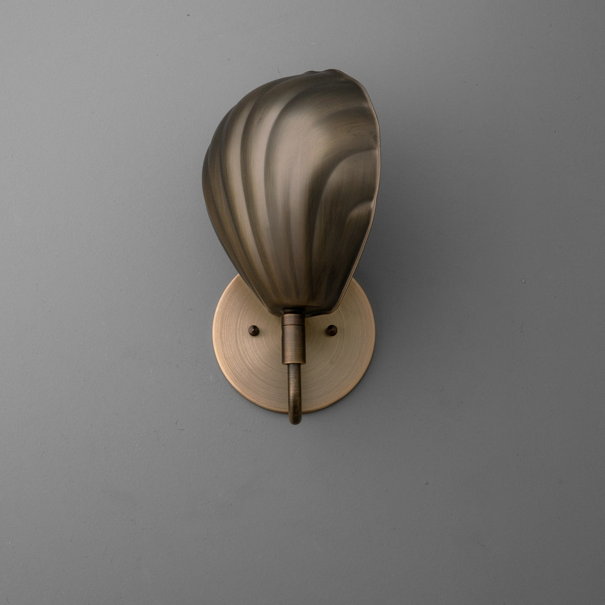Bronze wall sconce with a single bulb and a curved, shell-inspired metal shade mounted on a round base. - SCONCE MODEL NO. 1086