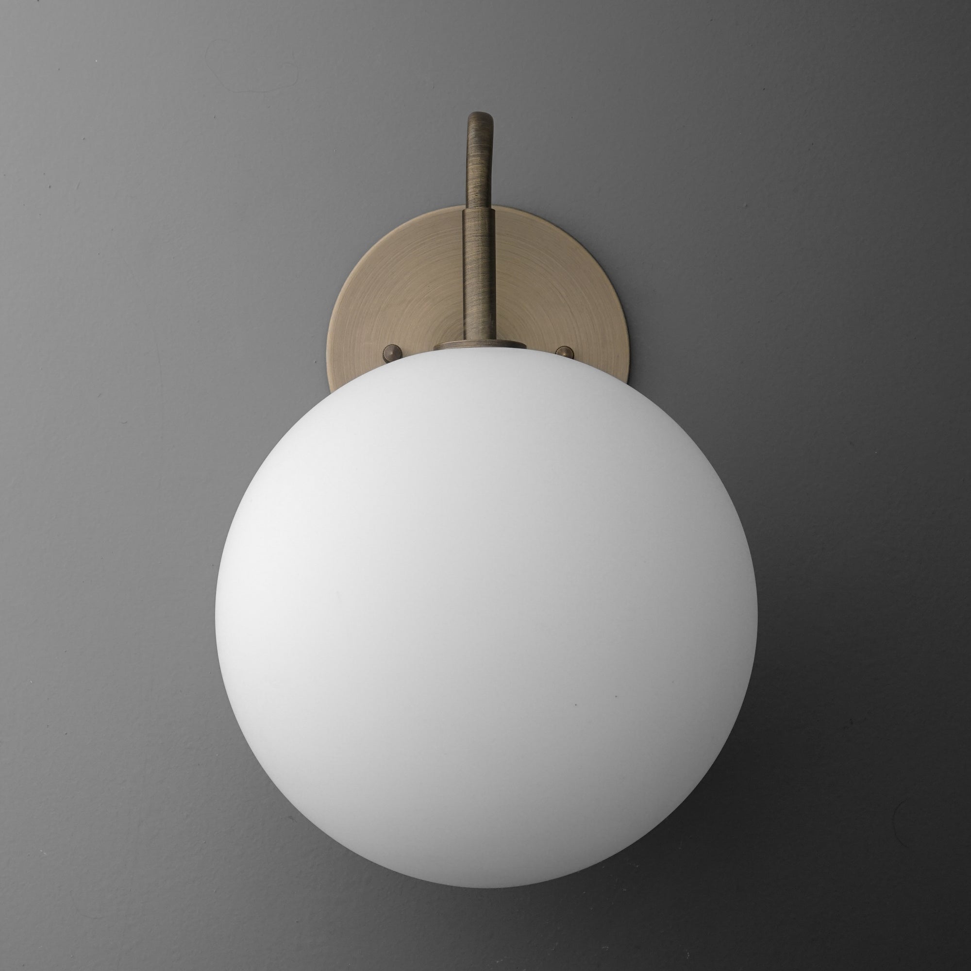 Minimalist wall sconce with frosted white globe and antique brass mount on gray background. - SCONCE MODEL NO. 0478