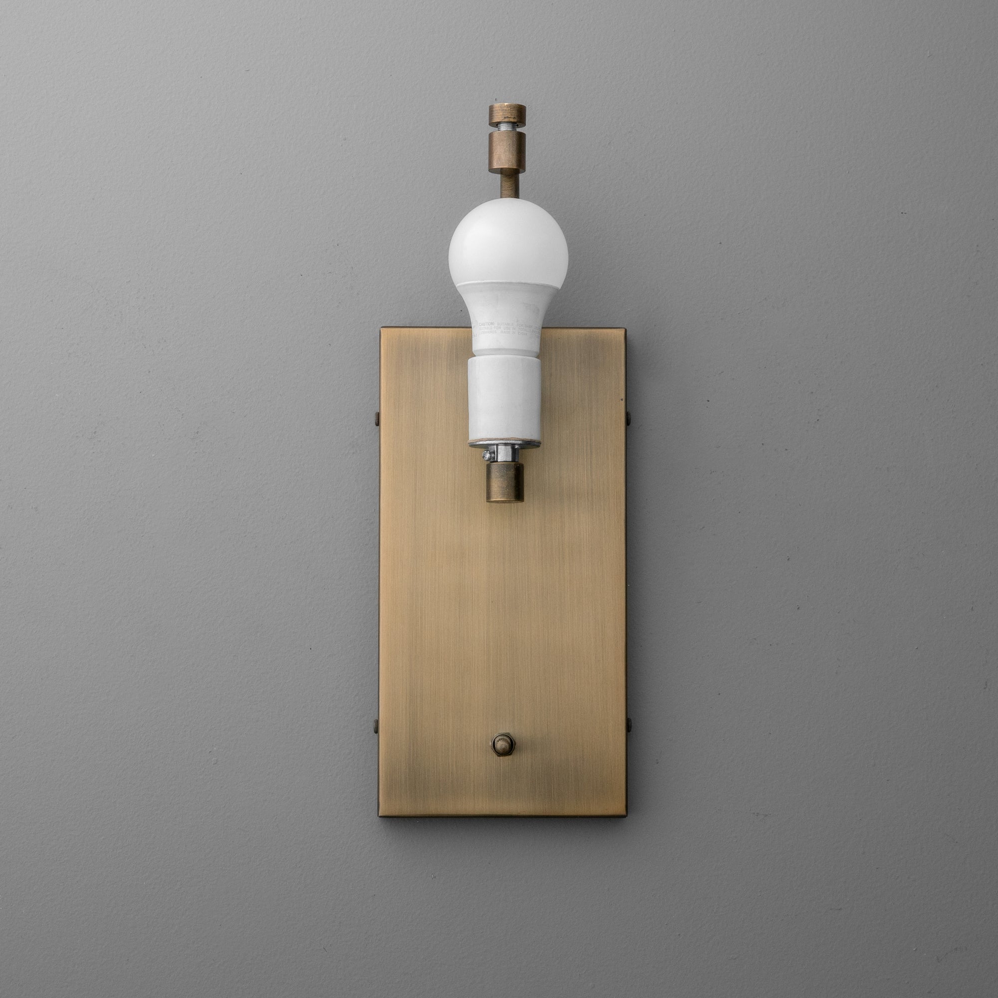 Antique brass wall sconce with rectangular backplate and exposed bulb on gray background. - SCONCE MODEL NO. 1918