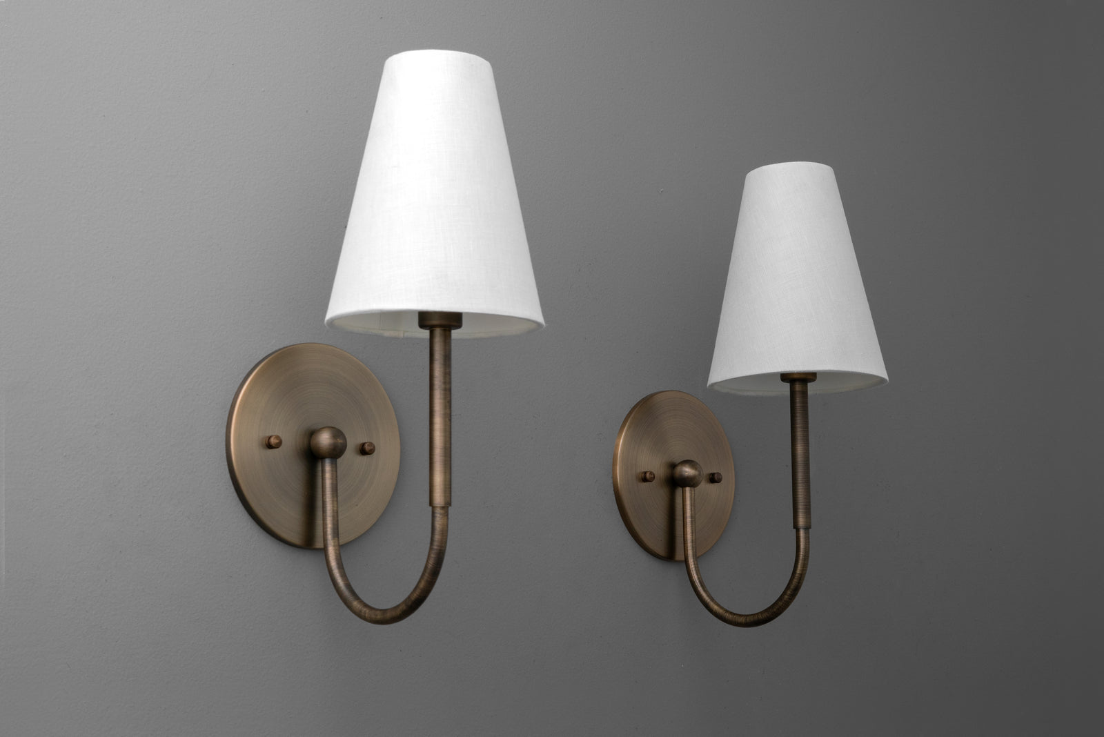Antique brass wall sconce with curved arm and white tapered fabric shade on gray background. - SCONCE MODEL NO. 4594