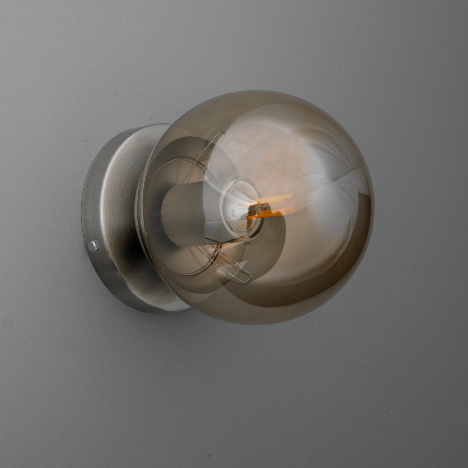 Wall sconce with a round smoked glass globe and brushed metal base, single bulb design. - SCONCE MODEL NO. 1030