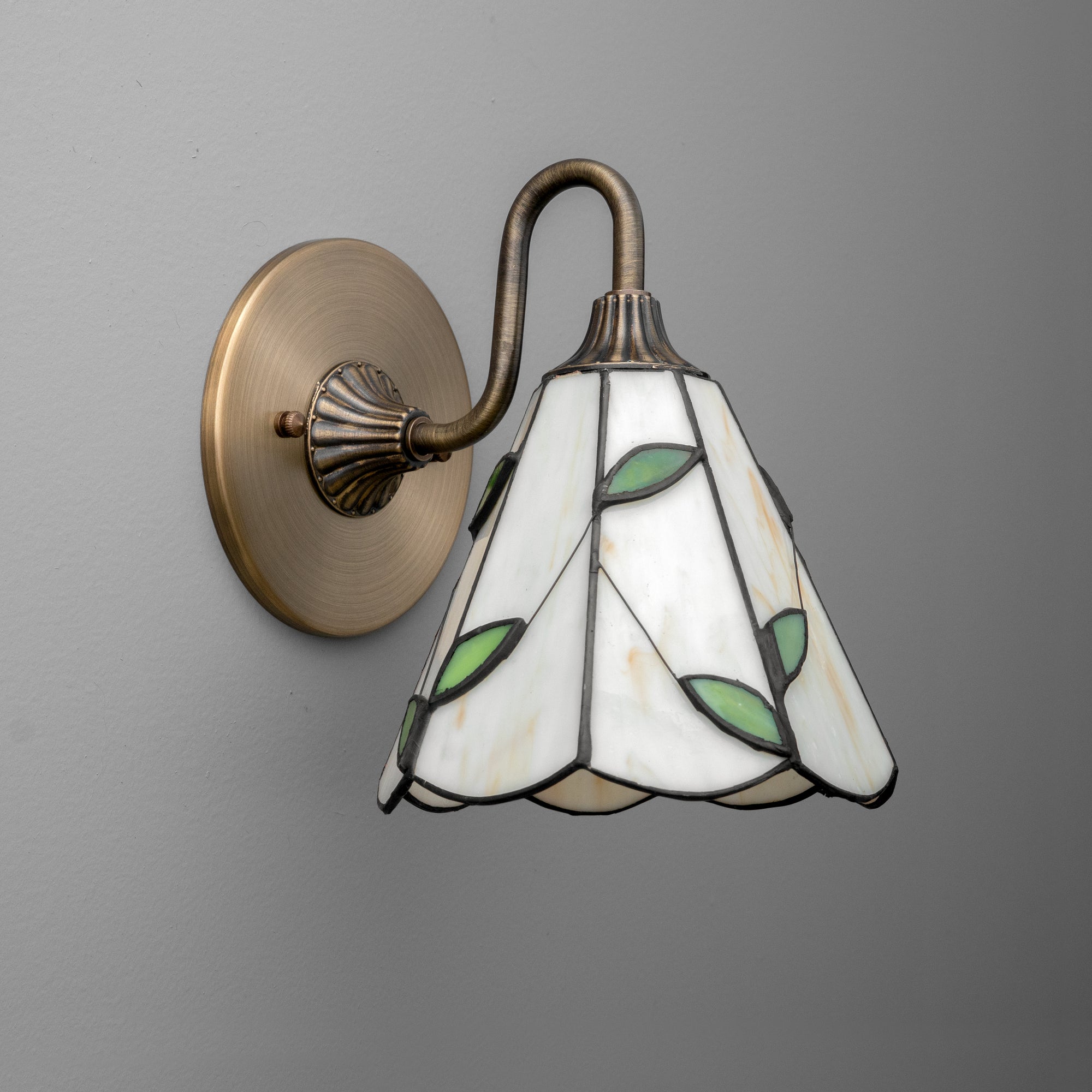 Wall sconce with antique brass finish and white stained glass shade featuring green leaf accents. - SCONCE MODEL NO. 8543