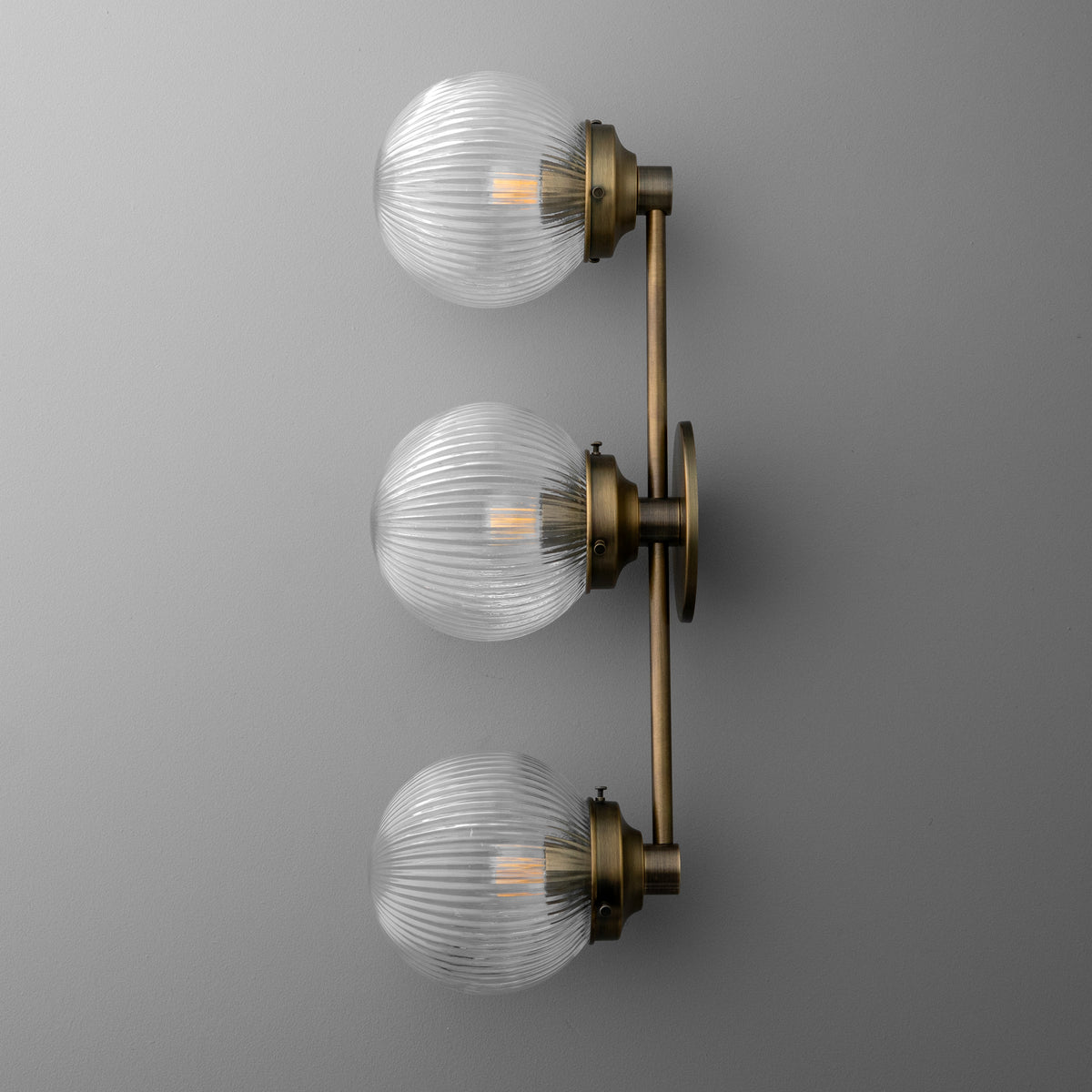 Three-bulb wall sconce with ribbed clear glass globes and antique brass finish on horizontal bar. - SCONCE MODEL NO. 1108