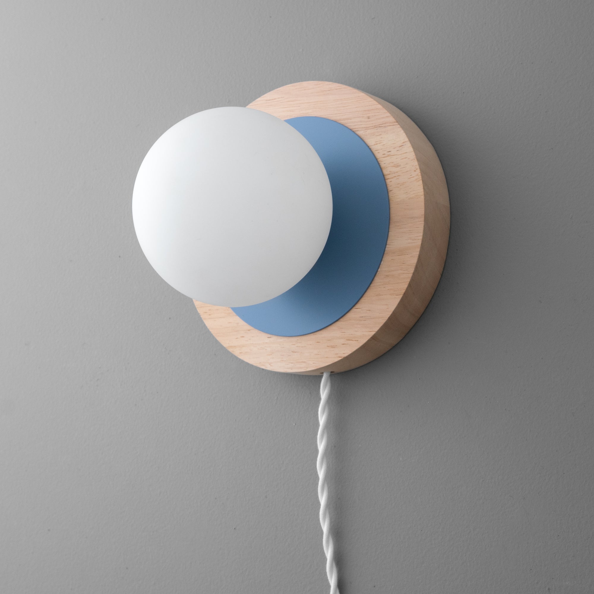 Wall sconce with frosted white glass globe, light wood backplate, and periwinkle blue accent on gray wall. - SCONCE MODEL NO. 6154