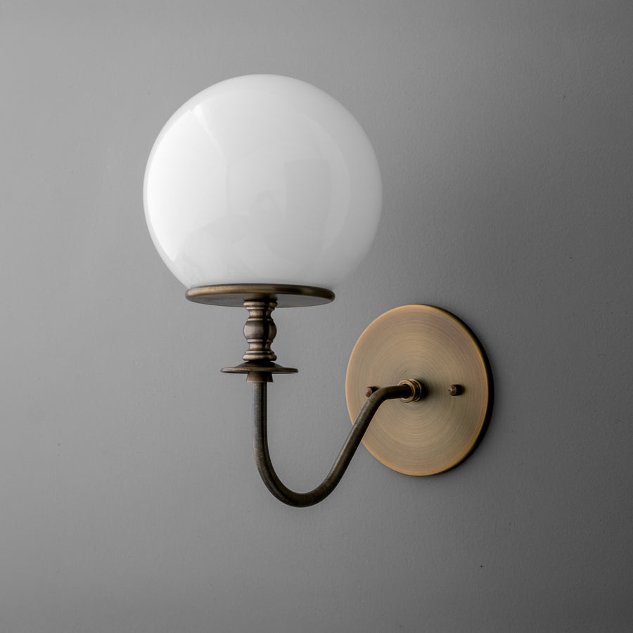 Wall sconce with antique brass finish featuring curved arm and white glass globe shade. - SCONCE MODEL NO. 7857