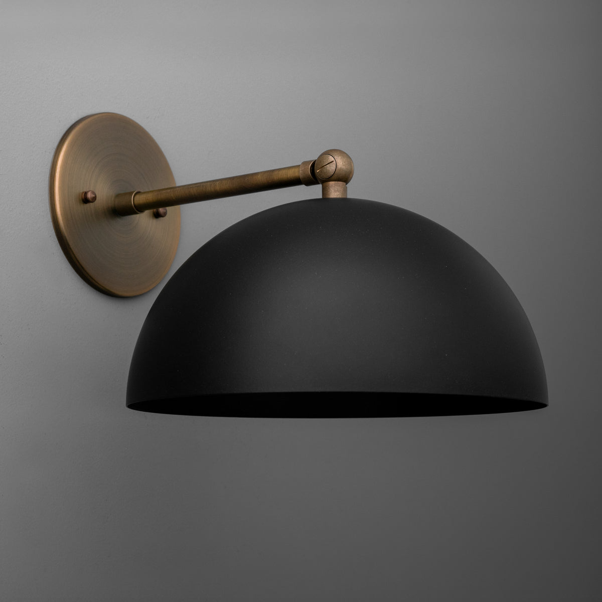 Single-light sconce in Antique Brass with a straight arm and swivel knuckle holding a wide steel dome shade, on a round wall plate. - SCONCE MODEL NO. 7212