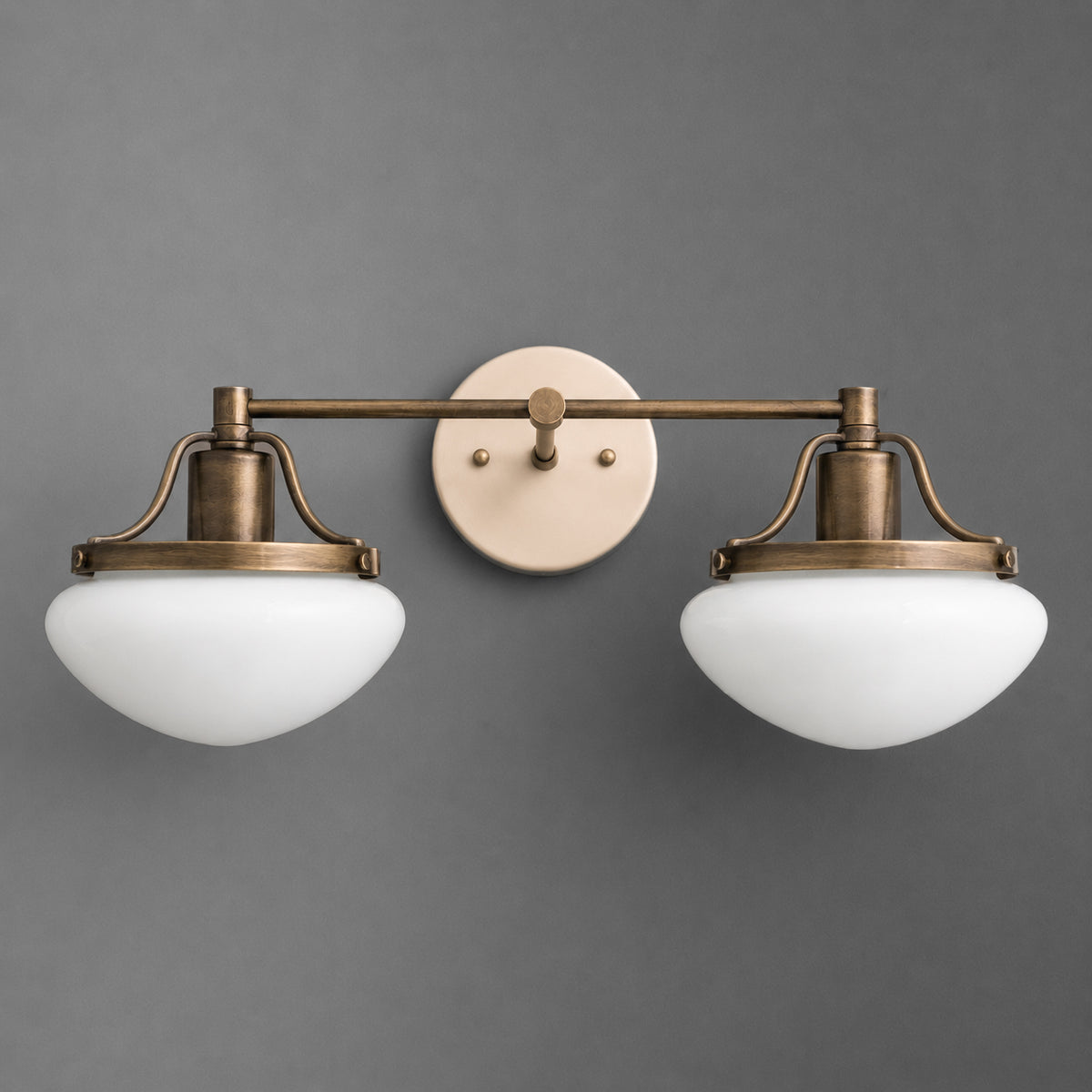 Two-light vanity light in Antique Brass with a Cream round wall plate and glass mushroom shades held in caged fitters on a straight bar. - VANITY LIGHT MODEL NO. 2448