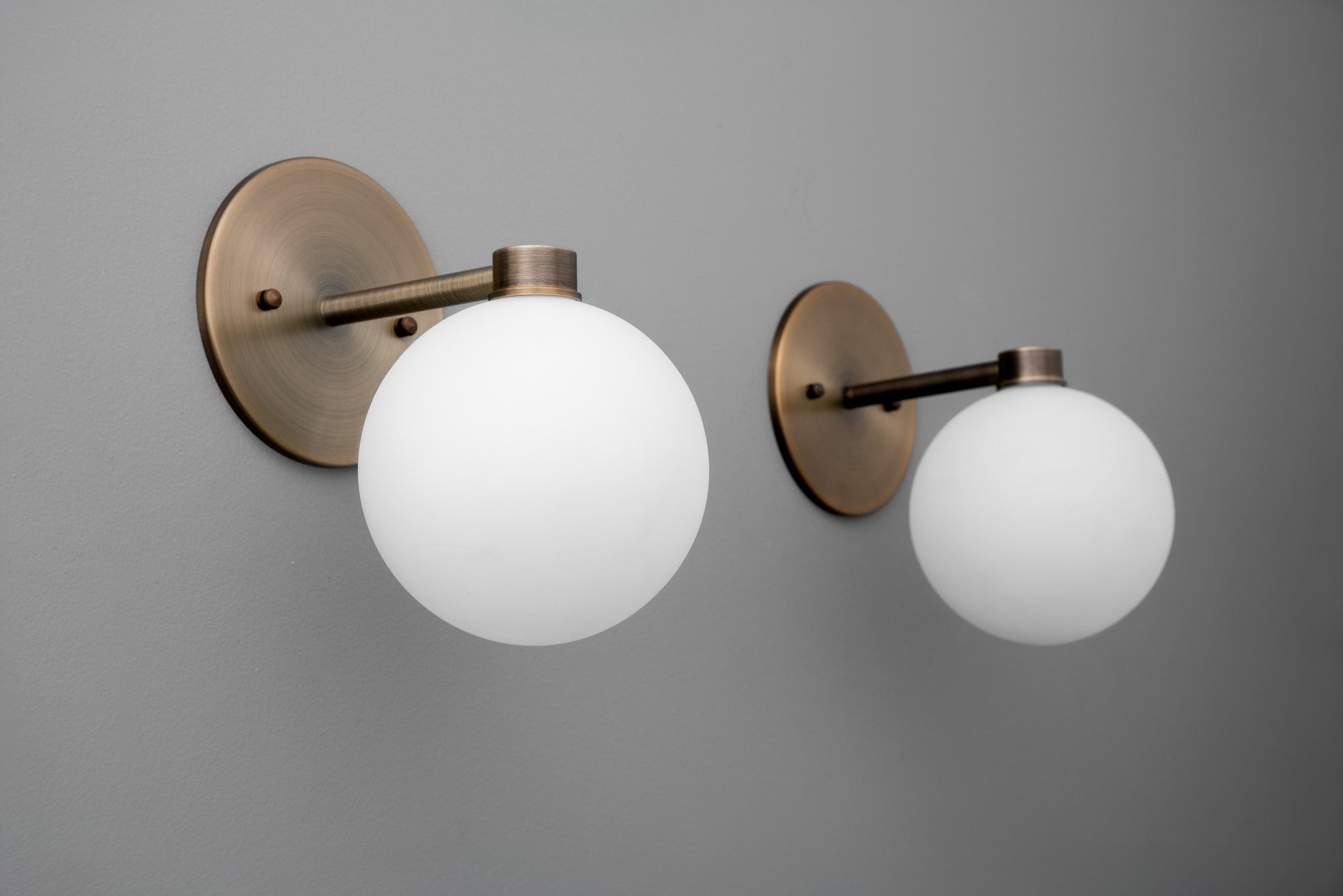 Pair of antique brass wall sconces with round white globe shades mounted on circular backplates. - SCONCE MODEL NO. 2341