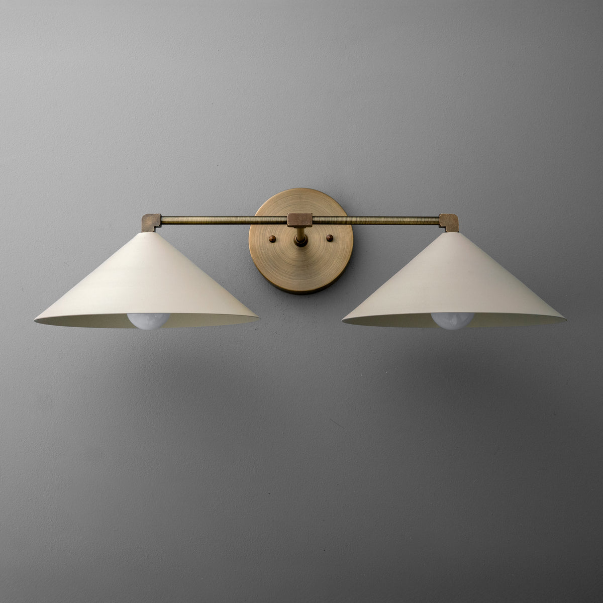 Two-light vanity light in Antique Brass with wide steel cone shades on a straight arm and a round wall plate. - VANITY LIGHT MODEL NO. 1185