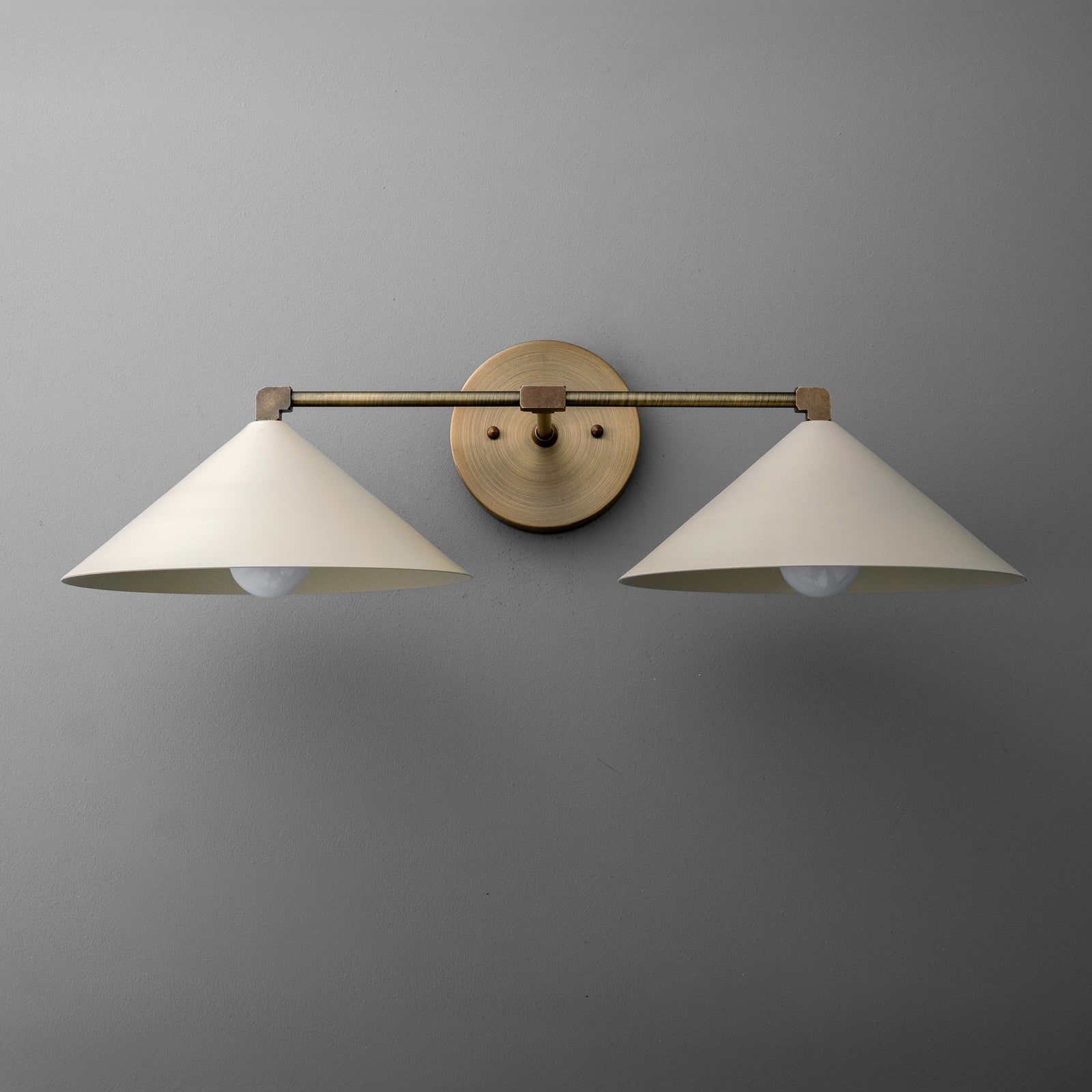 Two-light vanity light in Antique Brass with wide steel cone shades on a straight arm and a round wall plate. - VANITY LIGHT MODEL NO. 1185