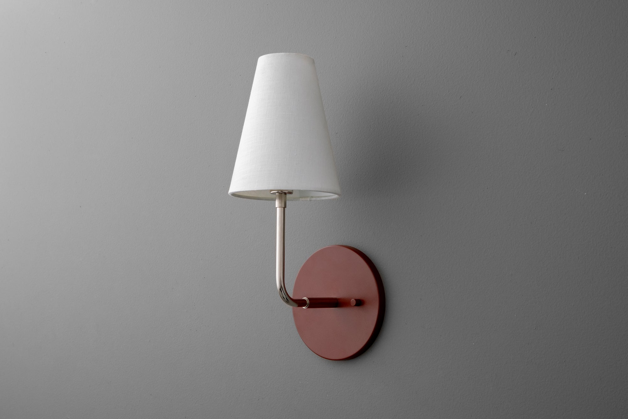 Wall sconce with polished nickel arm, round brick red base, and white tapered fabric shade. - SCONCE MODEL NO. 3928