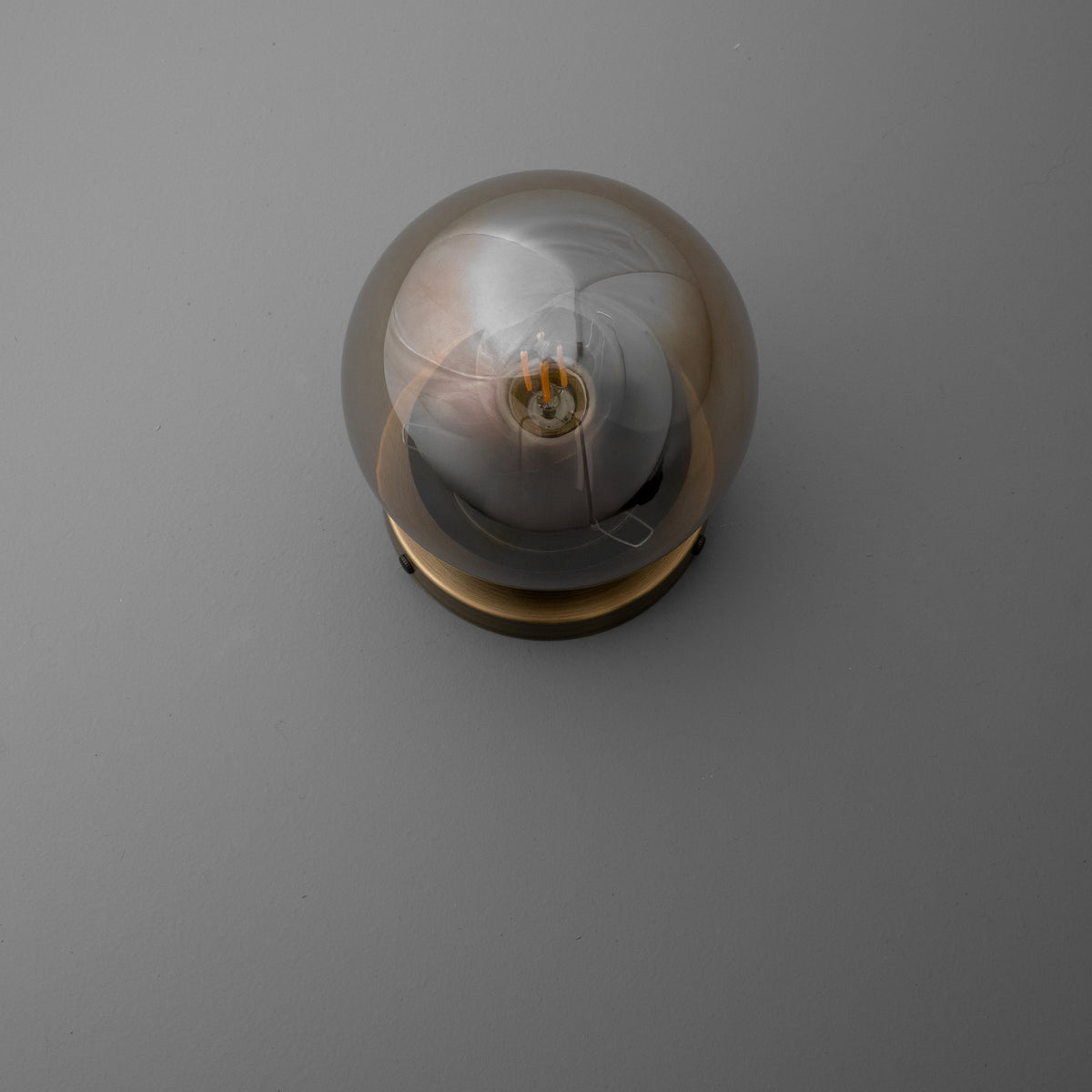 Round amber glass globe sconce with visible filament bulb and brass base on gray wall. - SCONCE MODEL NO. 1030
