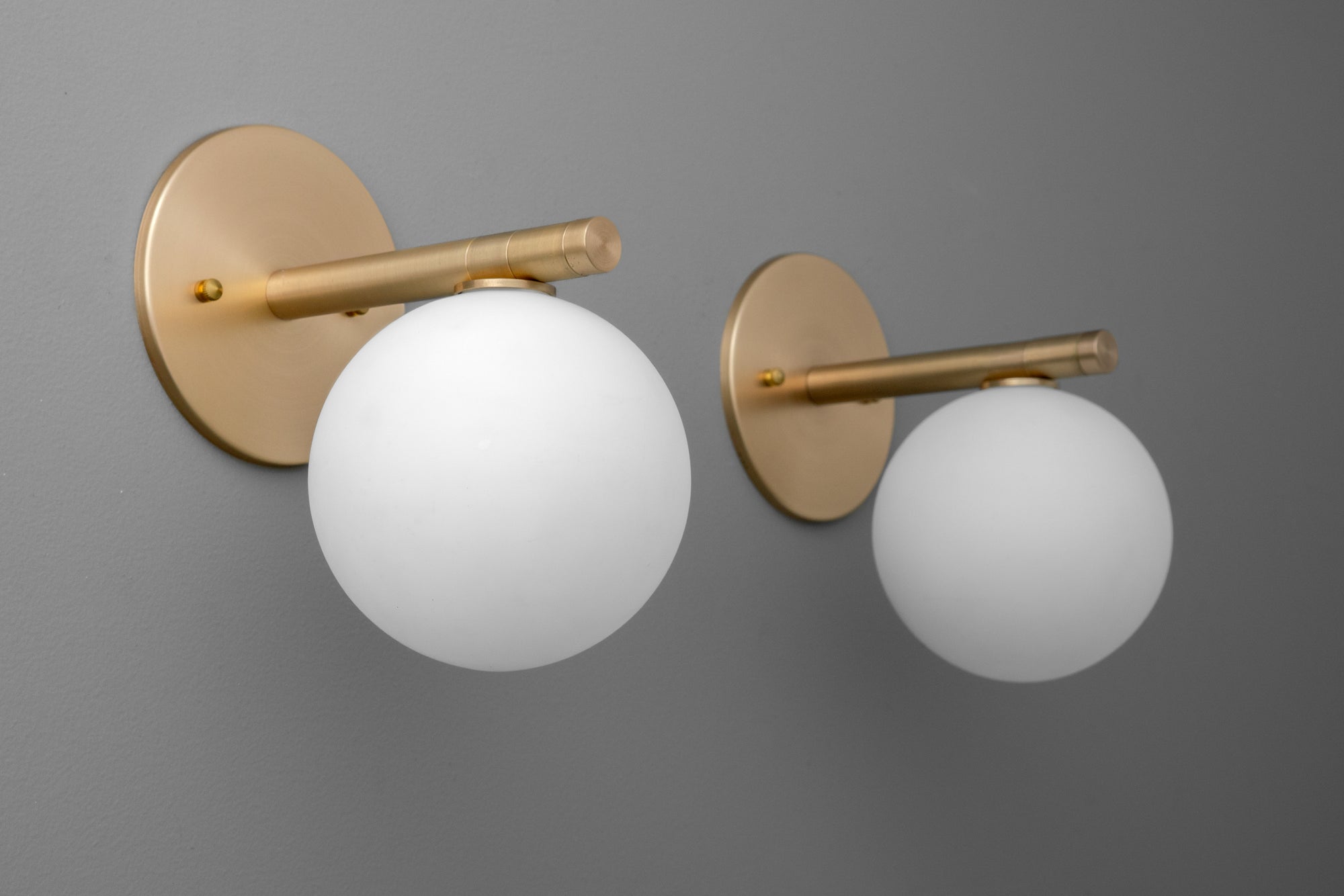 Pair of wall sconces with round white glass globes and raw brass fixtures against gray background. - SCONCE MODEL NO. 0904