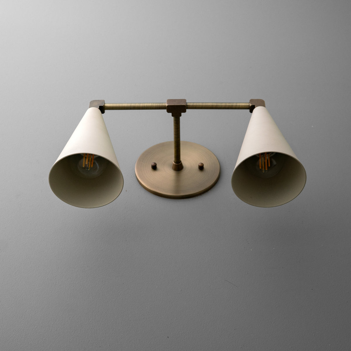 View from below of the vanity light in Antique Brass with Cream cone shades, showing the bulbs inside and the round wall plate. - VANITY LIGHT MODEL NO. 1184