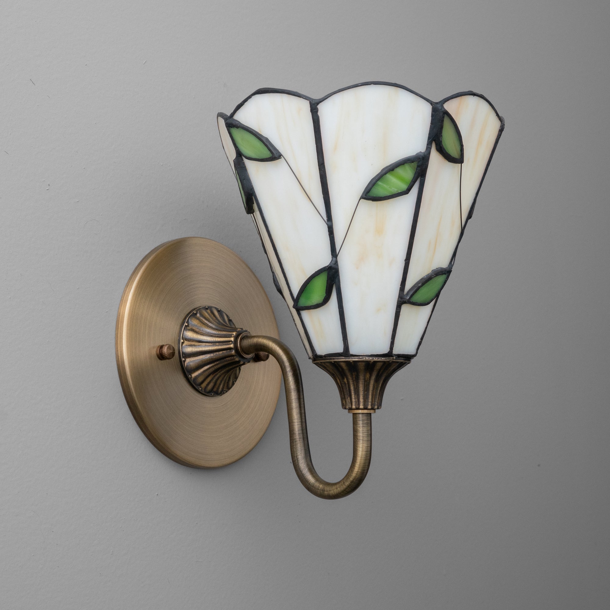 Wall sconce with antique brass finish and stained glass shade featuring white panels and green leaf accents. - SCONCE MODEL NO. 8543