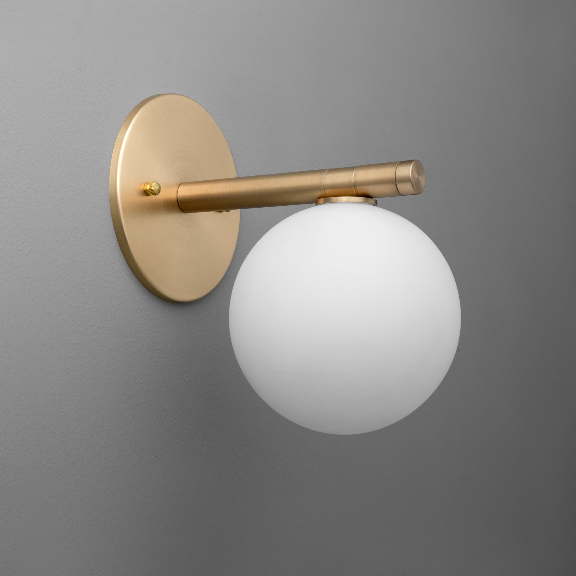 Wall sconce with raw brass finish and frosted white glass globe shade against a gray background. - SCONCE MODEL NO. 0904