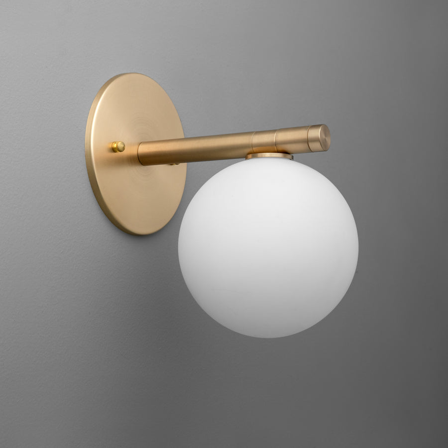 Wall sconce with raw brass finish and frosted white glass globe shade against a gray background. - SCONCE MODEL NO. 0904