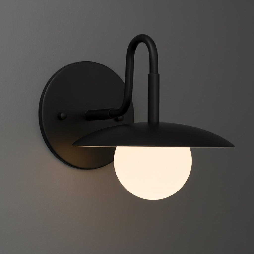 Matte black metal wall sconce with curved arm and flat circular shade over frosted white glass globe bulb. - SCONCE MODEL NO. 1078