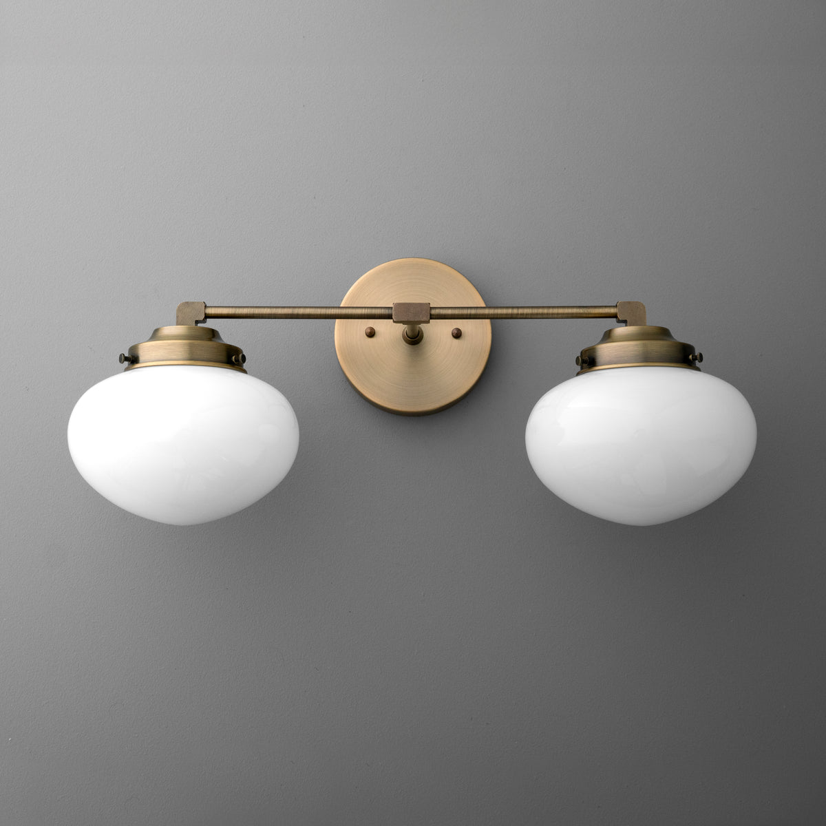 Two-bulb vanity light with round white glass shades and antique brass finish mount and arm. - VANITY LIGHT MODEL NO. 1167