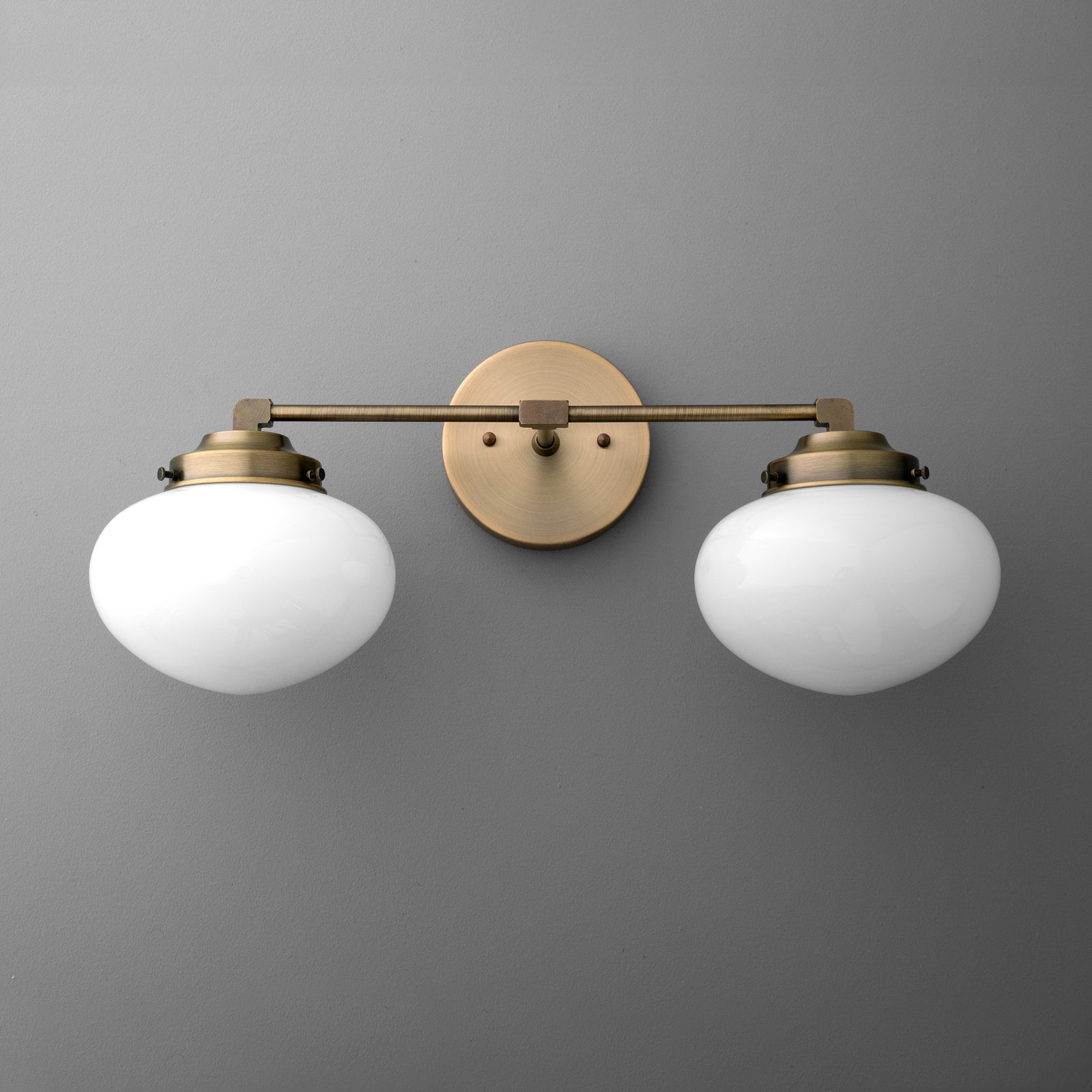 Two-bulb vanity light with round white glass shades and antique brass finish mount and arm. - VANITY LIGHT MODEL NO. 1167