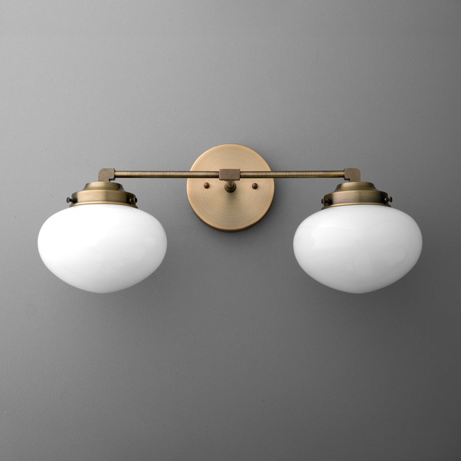Two-bulb vanity light with round white glass shades and antique brass finish mount and arm. - VANITY LIGHT MODEL NO. 1167