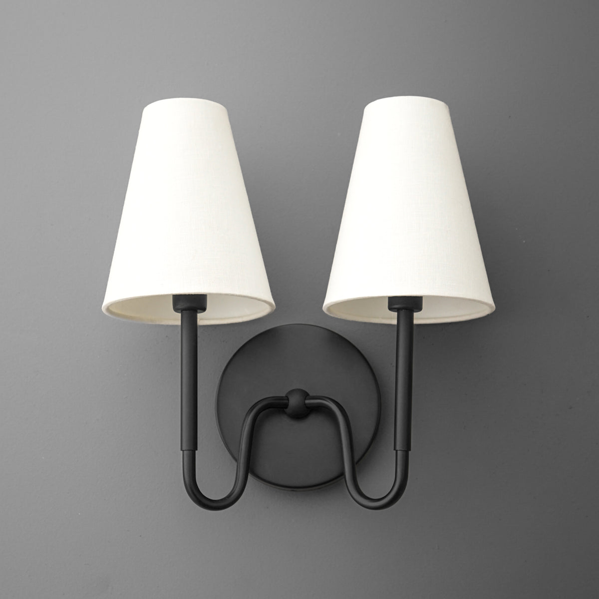 Black metal double-arm wall sconce with round base and white tapered fabric shades. - SCONCE MODEL NO. 5265