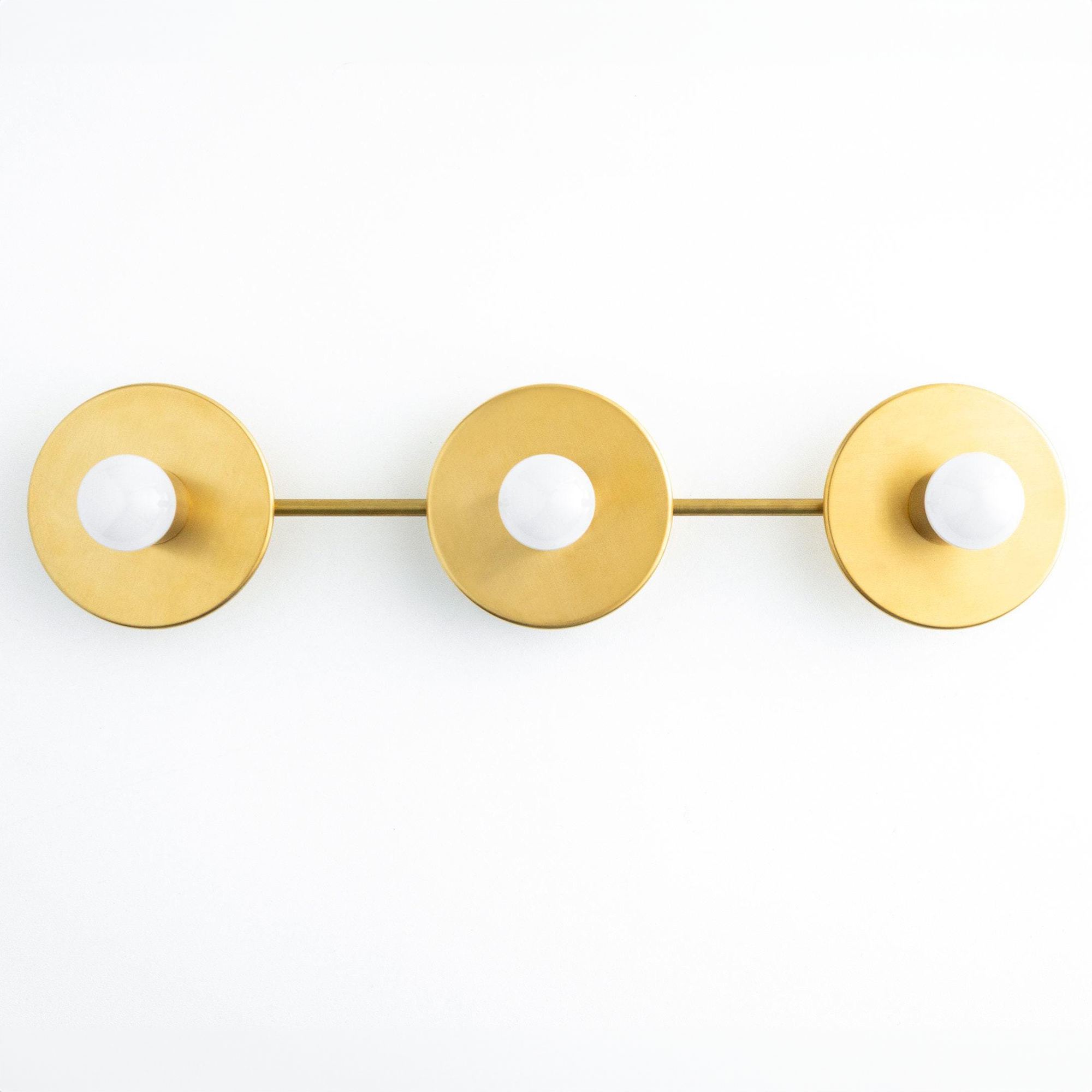 Mid-century modern vanity light with three round antique brass fixtures and exposed bulbs on a horizontal bar. - VANITY LIGHT MODEL NO. 5708