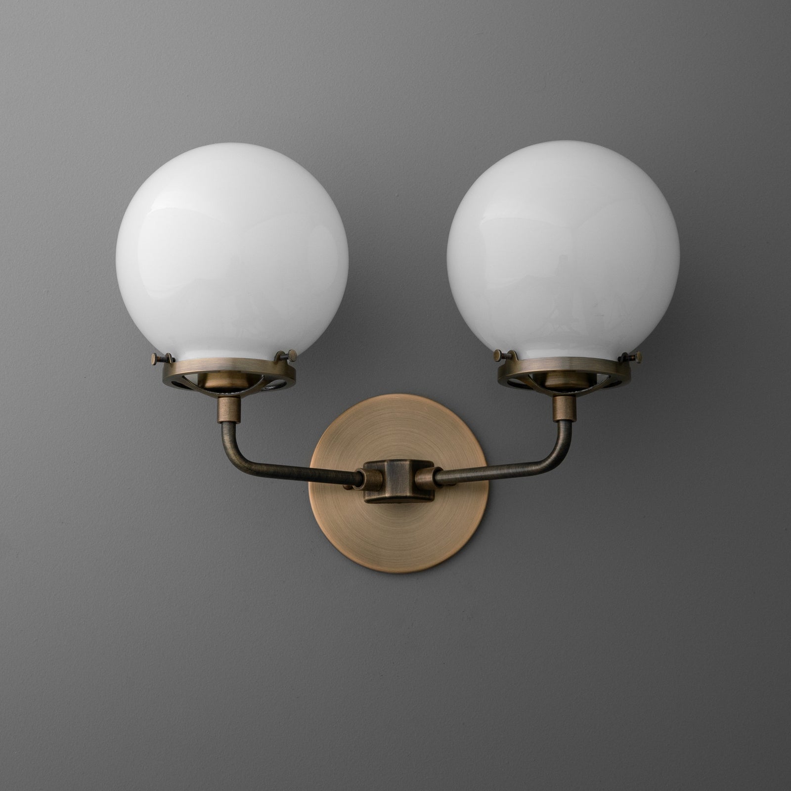 Double-bulb wall sconce with round white glass shades and antique brass finish on curved arms and circular backplate. - SCONCE MODEL NO. 9912