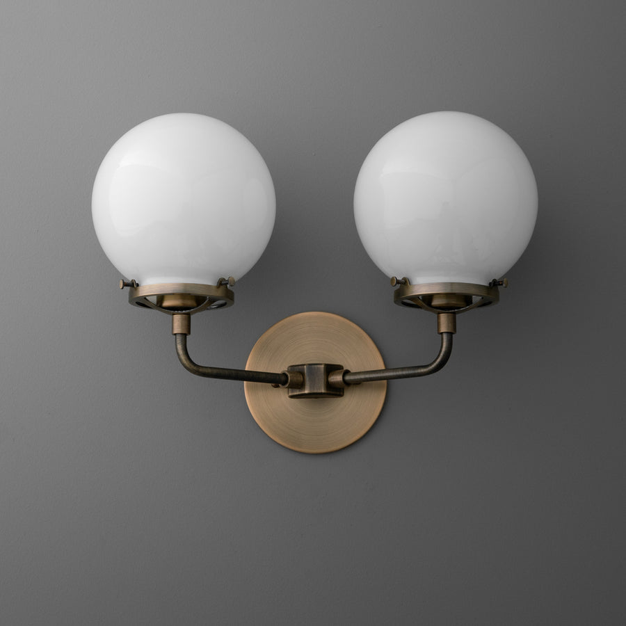 Double-bulb wall sconce with round white glass shades and antique brass finish on curved arms and circular backplate. - SCONCE MODEL NO. 9912