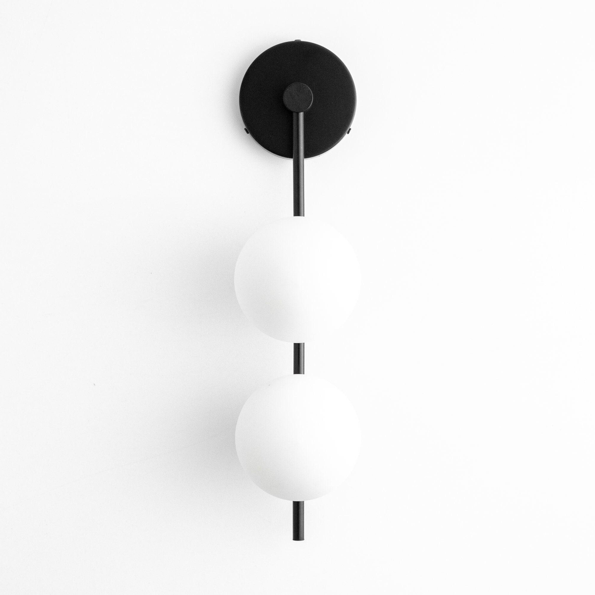 Black metal wall sconce with two white frosted glass globes stacked vertically on a slender rod. - SCONCE MODEL NO. 0344